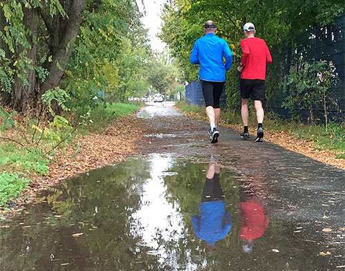 Läufer spiegeln sich in großer Regenpfütze